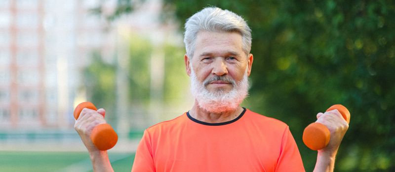 Aging with Power Elderly man lifting orange dumbbells outdoors, showcasing fitness and vitality